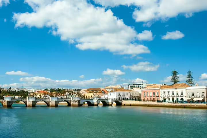 Picturesque view of Tavira's Roman bridge and colorful buildings under a vibrant blue sky, Algarve, Portugal self-drive tour.