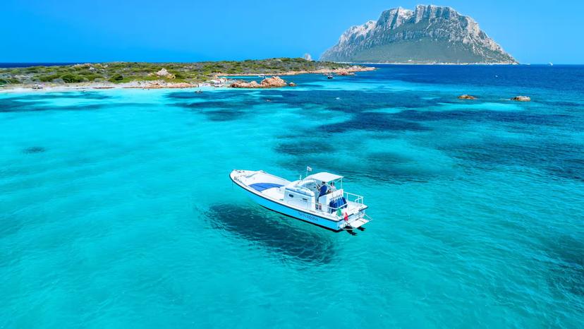 Pristine blue waters around Tavolara Island with a boat anchored nearby, ideal for a scenic Porto San Paolo tour.