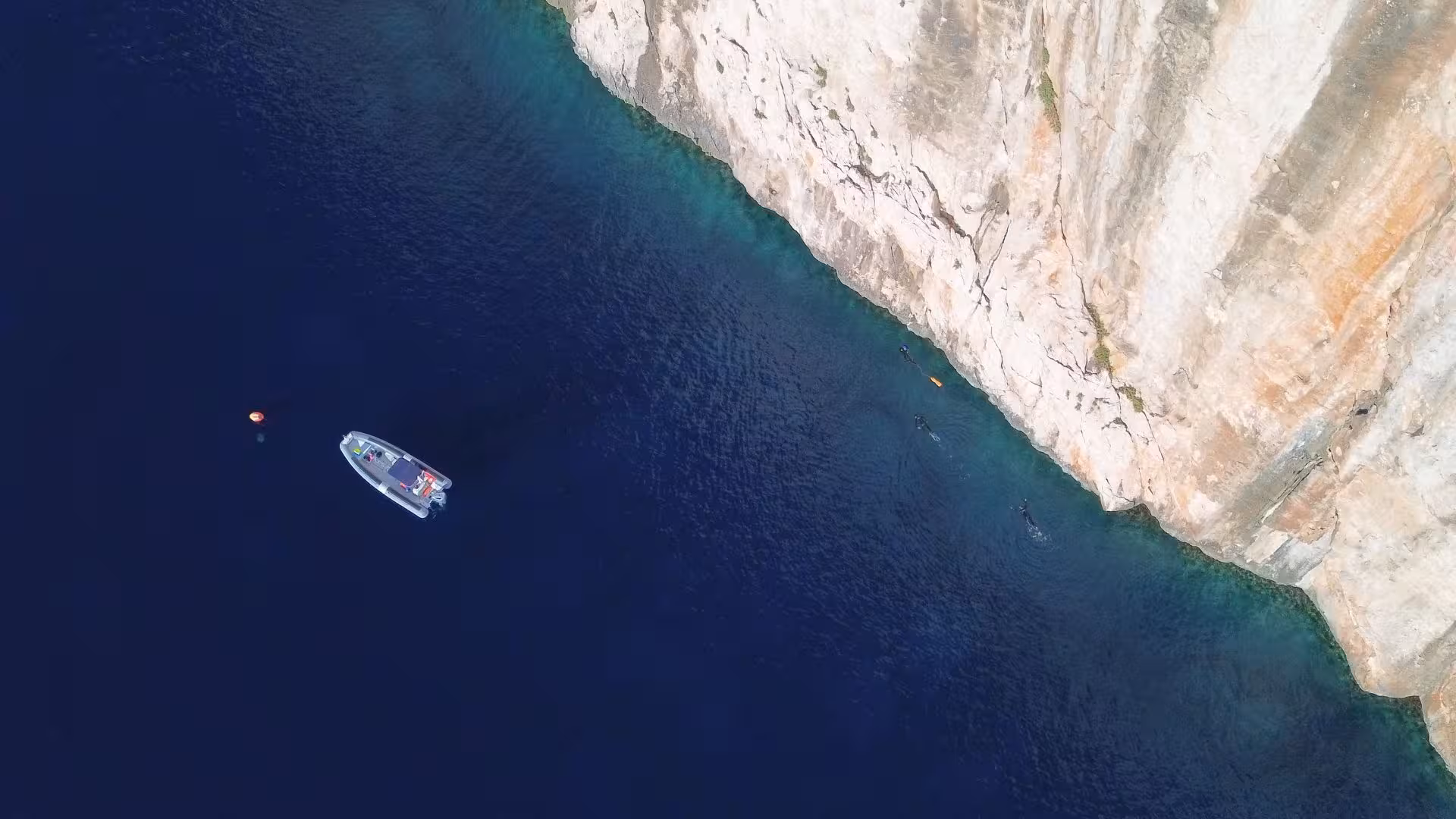 Boat anchored near the towering cliffs of Tavolara Island, with snorkelers enjoying the deep blue waters on a San Teodoro tour.