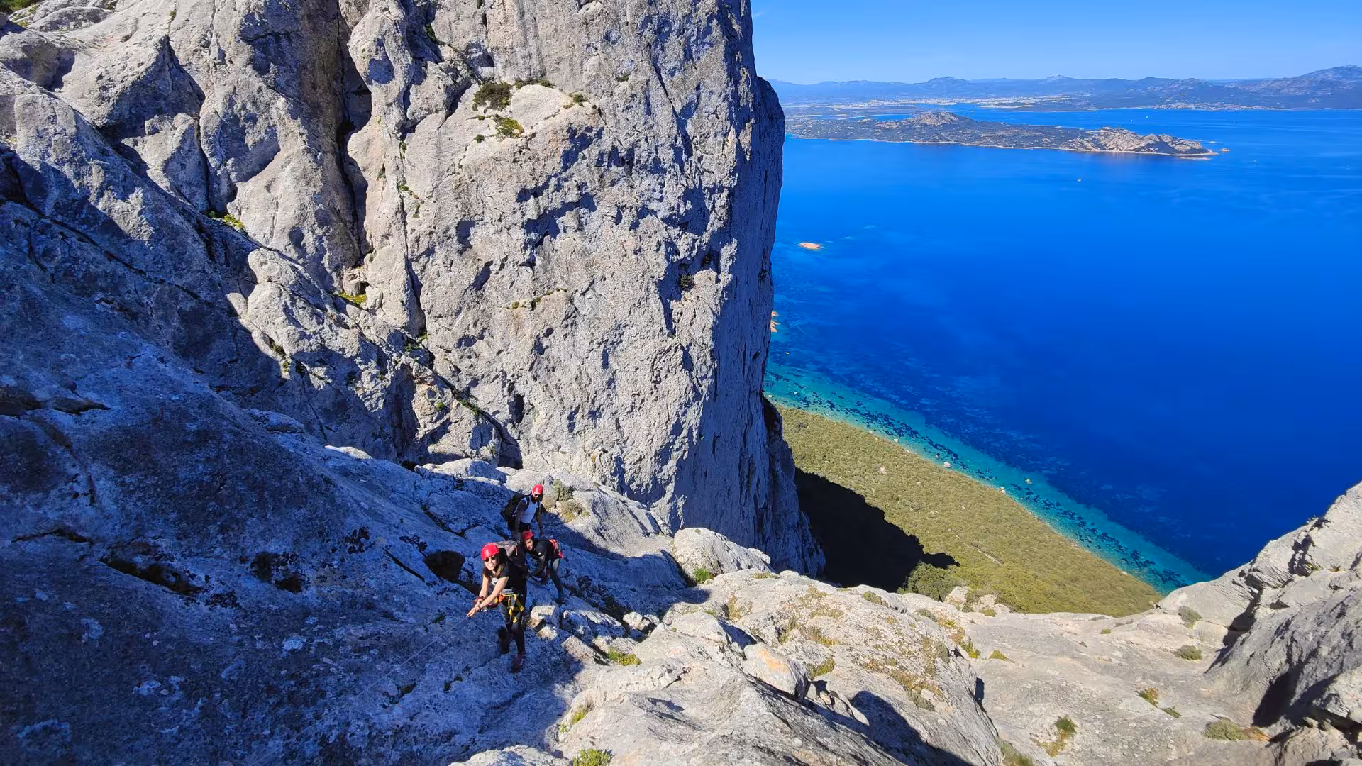 Adventurers climb steep rock faces on Tavolara Island, overlooking the stunning coastline near Porto San Paolo.
