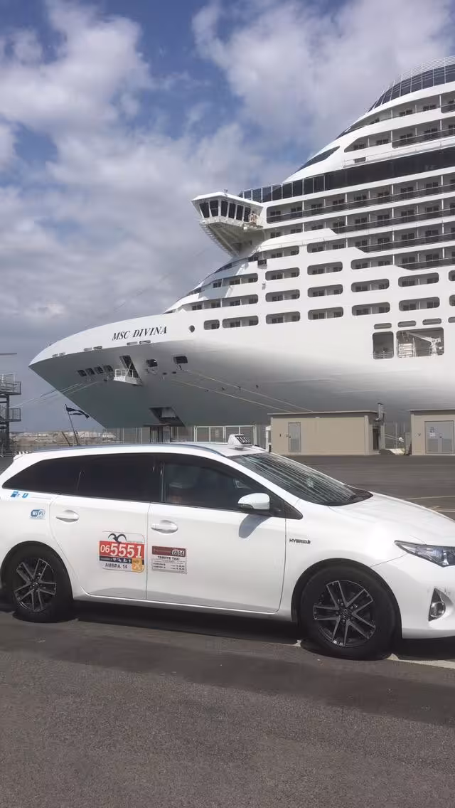 White taxi parked near MSC Divina cruise ship at Civitavecchia port, offering transfers to Fiumicino airport.