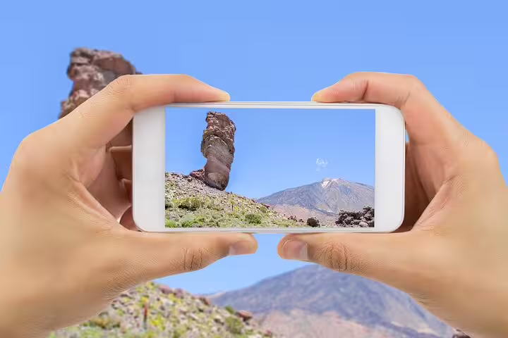 Hands holding smartphone capturing iconic rock formations and Mount Teide in Teide National Park.