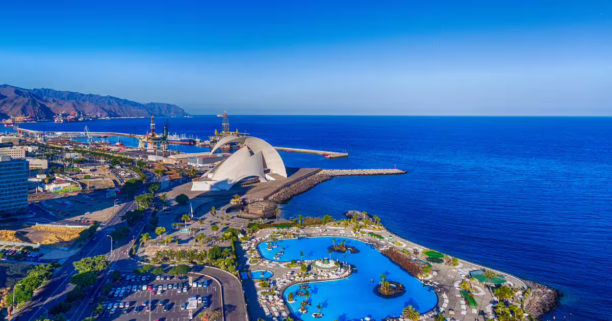 Stunning aerial view of Tenerife's Auditorio de Tenerife by the ocean with bright blue skies and mountain backdrop.