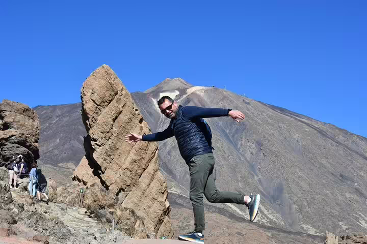 Man balancing playfully near Teide Volcano, showcasing stunning rock formations and clear blue skies.