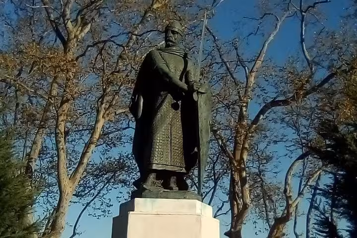 Statue of a Templar knight in historical attire surrounded by bare trees under a clear blue sky.