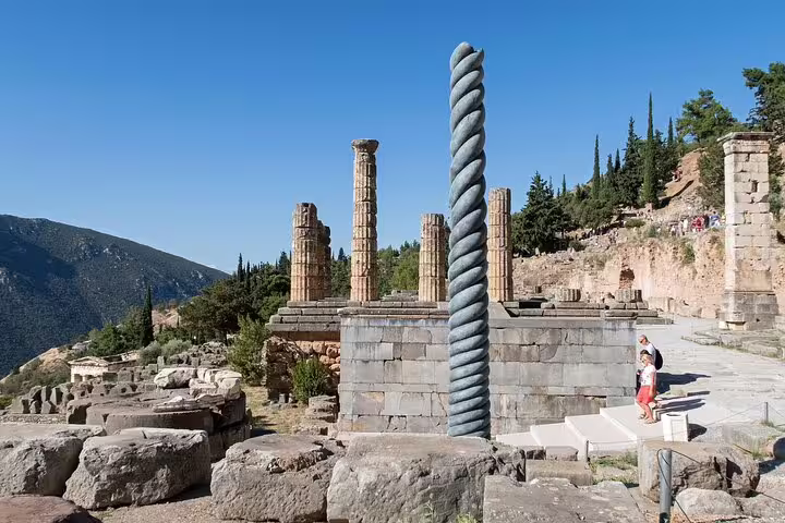 Ruins of the Temple of Apollo in Delphi with iconic spiral column under a clear blue sky on Athens tour.