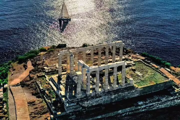 Temple of Poseidon at Cape Sounio above the sea with sailboat, ideal stop on a private Athens Riviera tour
