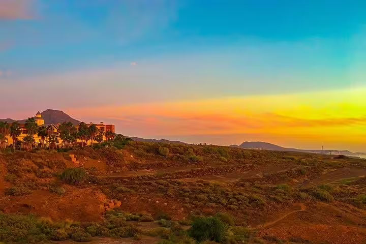 Vibrant sunset over Tenerife Island's rugged landscape with palm trees and distant mountains, ideal for sunset tours.