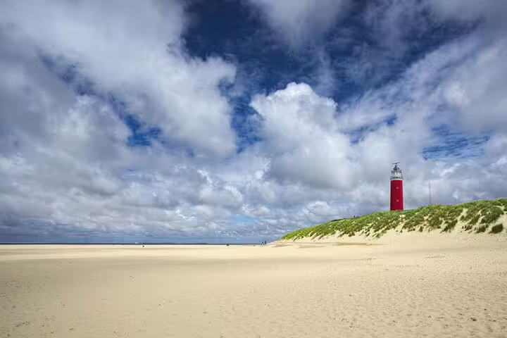 Red Texel lighthouse on wide sandy beach under dramatic clouds, highlight of a guided Texel day tour in Holland