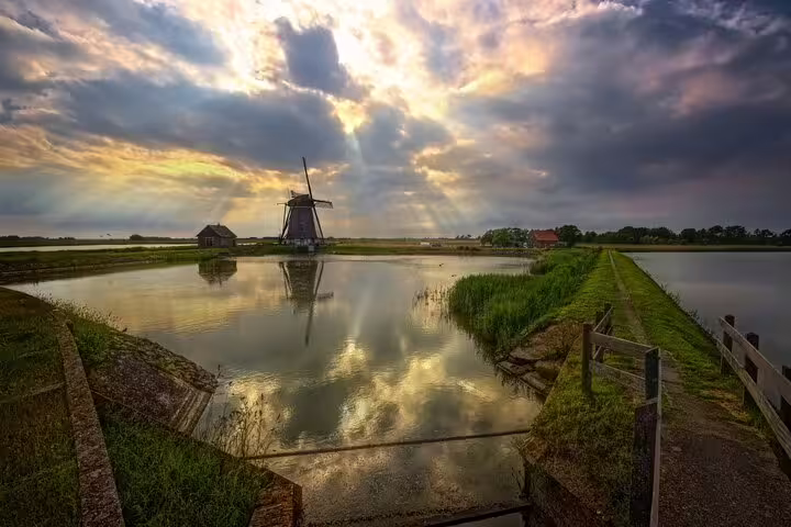 Windmill by tranquil dike canal at sunset on Texel Island, Netherlands, scenic stop on guided day tour