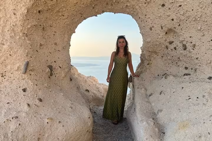Traveler in volcanic cave arch overlooking Santorini caldera on Island of Thera 8-hour tour with wine tasting