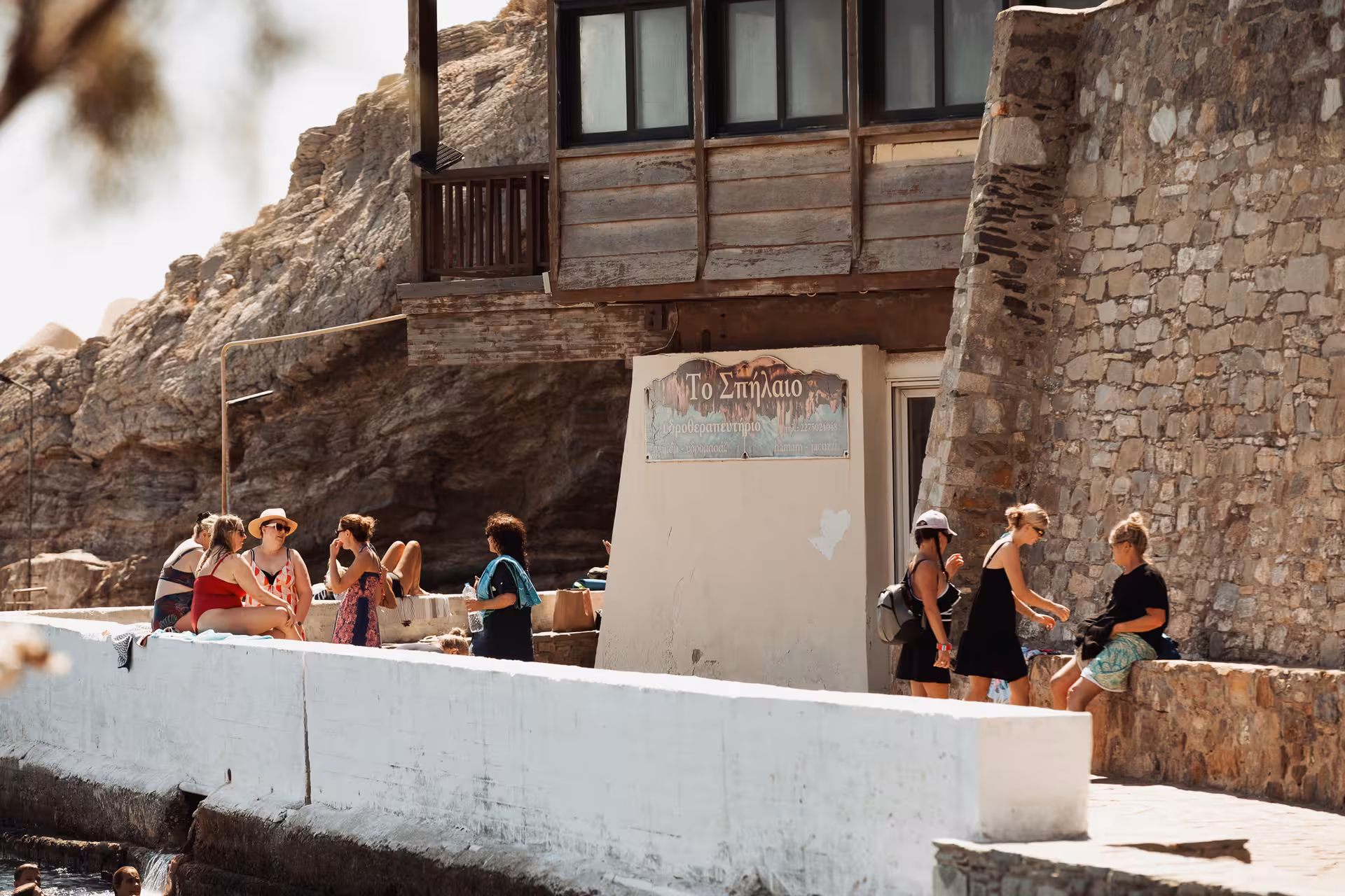 Travelers relax by the historic Therma hot springs in Ikaria, exploring stone village architecture on a sunny Aegean coast tour