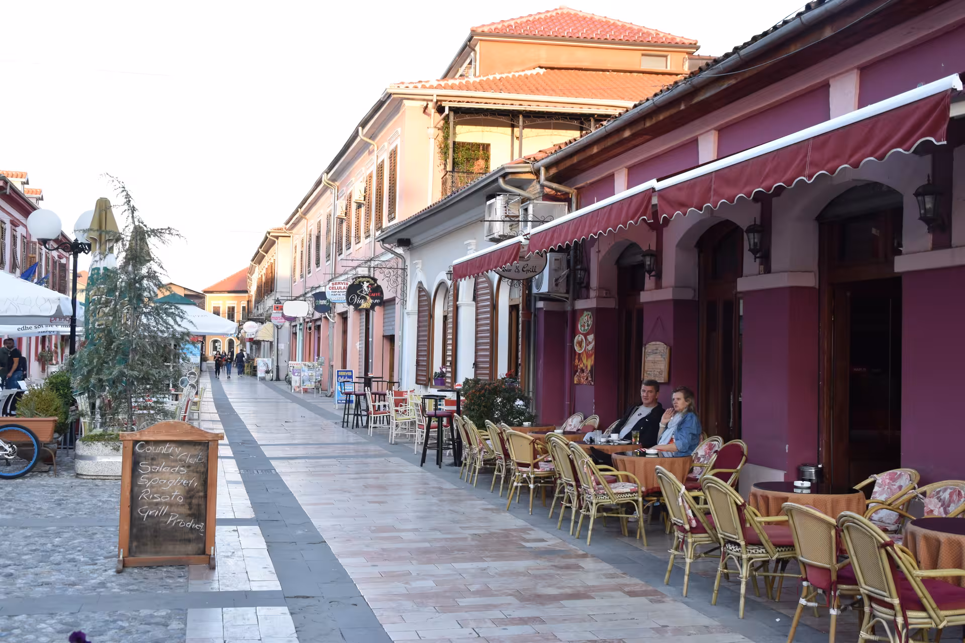 Charming street in Theth with outdoor cafes and colorful architecture, perfect for the Theth – Valbone Tour.
