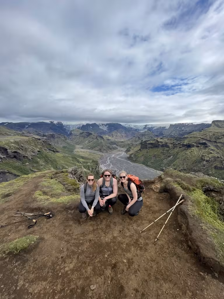 Three women hikers resting on a Þórsmörk trail, surrounded by dramatic landscapes and lush green valleys.