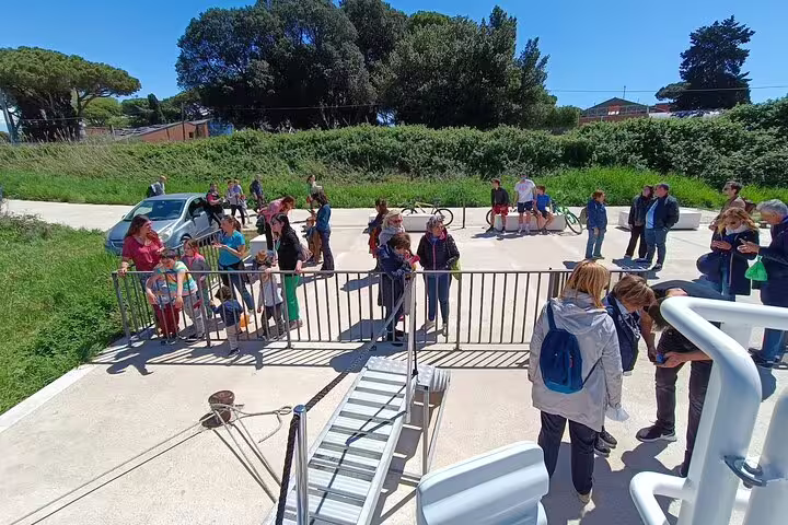 Tourists boarding the Tiber River cruise to Ancient Ostia from Rome, waiting by the gangway on a bright, clear day