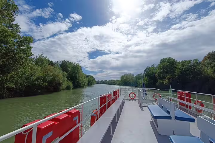 Sunny Tiber River cruise boat from Rome to Ancient Ostia, showing open deck seating, life rings and lush green riverbanks