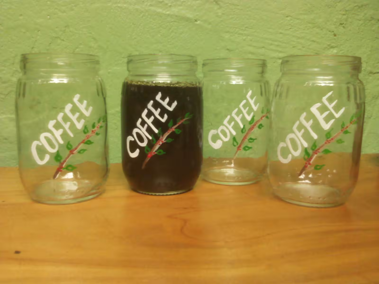 Four glass jars labeled 'Coffee,' one filled with brew, on display at Tierra Amiga Coffee Tour in San Marcos.