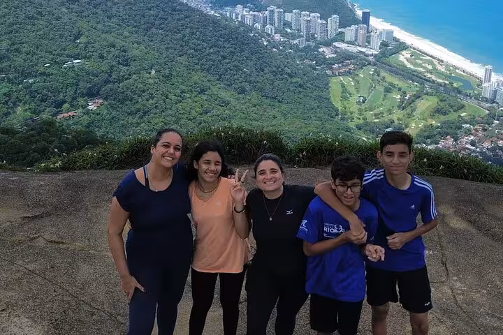 Group poses for a picture with scenic backdrop of Tijuca Forest and coastline, showcasing vibrant green landscape.