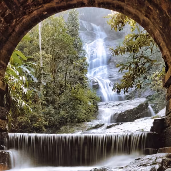 Lush waterfall view through a stone arch in Tijuca Forest, highlighting natural beauty on a private tour.