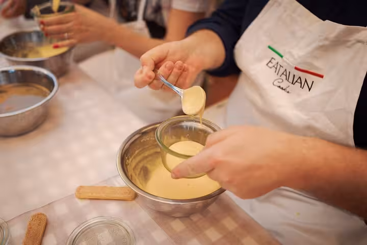 Participant prepares creamy tiramisu mixture during a cooking class in Rome's Piazza Navona.