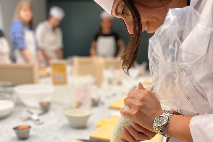 Close-up of a woman piping tiramisù cream during a hands-on Italian dessert and pasta-making workshop.