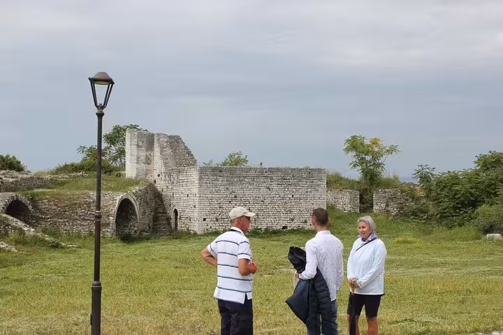 Tourists explore ancient stone ruins on a grassy field during the Tirana to Berat city tour in Albania.