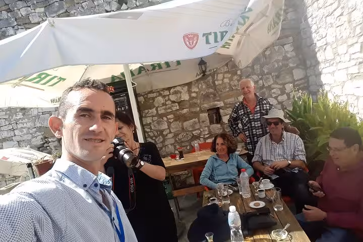 Tourists enjoying coffee under a shaded umbrella at a quaint café in Berat, Albania during the city tour and cooking class.