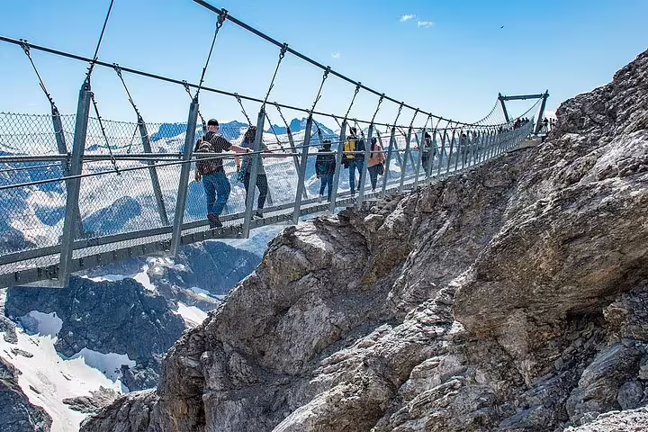 Tourists crossing the Titlis Cliff Walk suspension bridge with stunning Alpine views on Zurich small group tour.