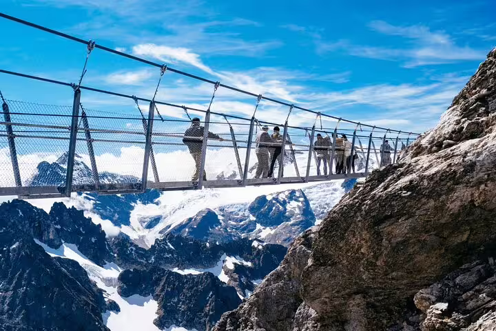 Tourists on the thrilling Titlis Cliff Walk bridge, offering stunning views of the Swiss Alps and rugged landscapes.