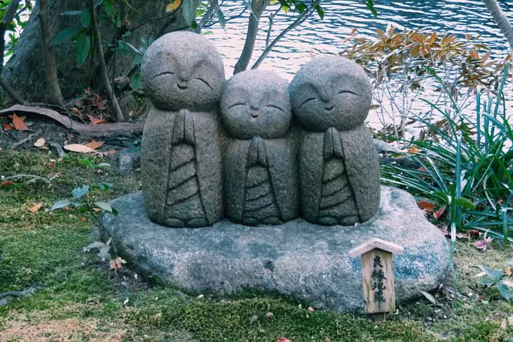 Three stone Jizo statues nestled in lush greenery, a serene stop on the Tokyo to Kamakura English Guided Tour.