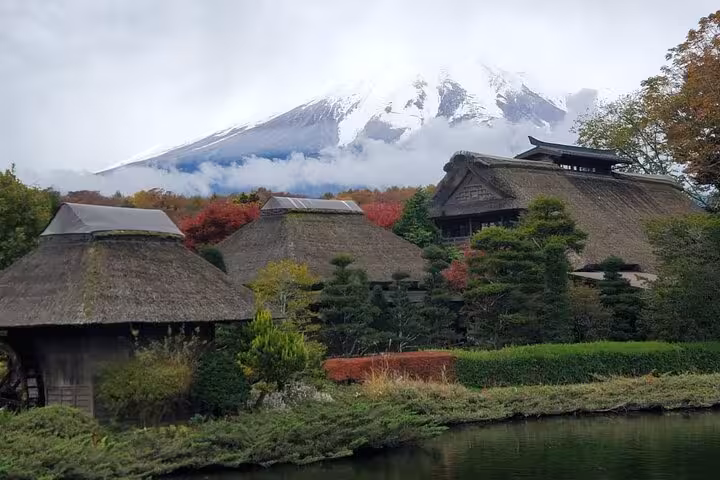 Traditional thatched-roof houses with Mt. Fuji backdrop surrounded by autumn foliage on customizable Tokyo tour.