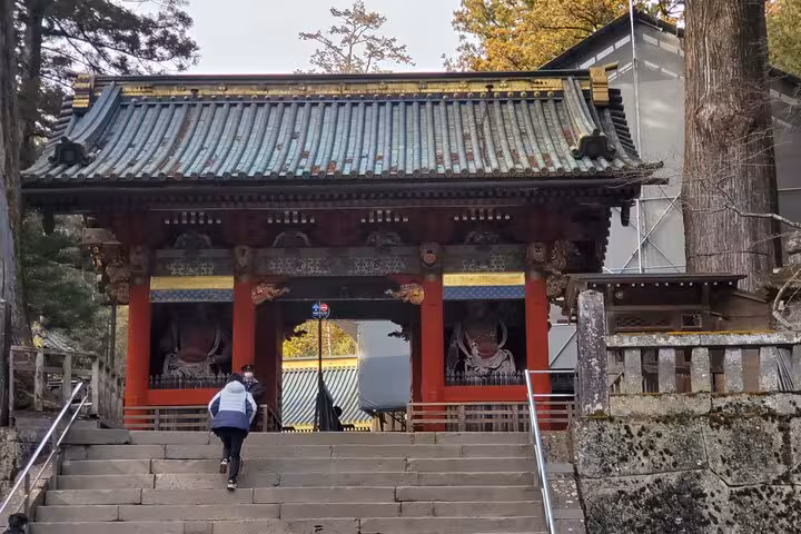 Visitors ascending the steps of a beautifully crafted traditional gate in Nikko, part of a Tokyo to Nikko guided tour.