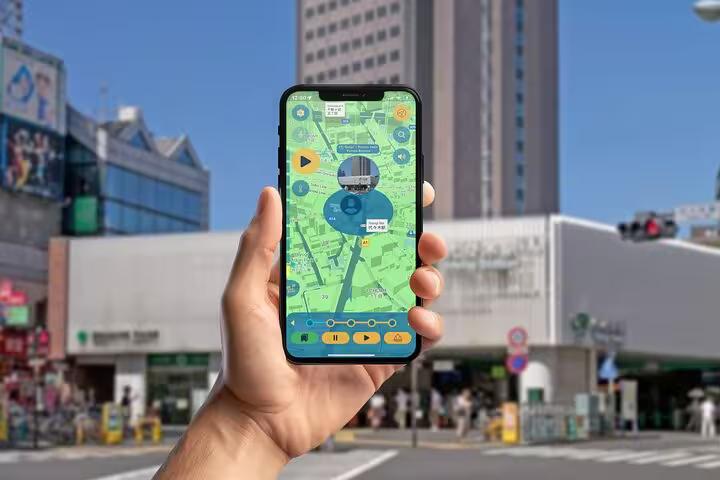 Hand holding phone with self-guided Tokyo walking tour app showing Meiji to Shibuya street navigation map