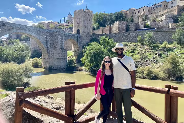 Tourists enjoying a scenic view of Toledo's historic bridge and architecture during a sunny Don Quixote tour.