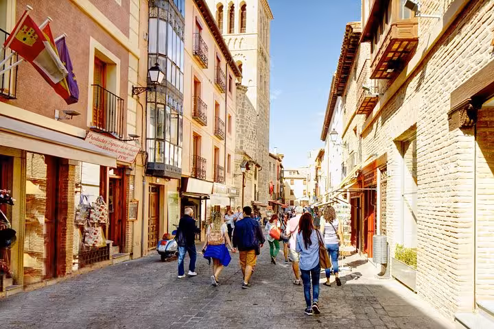 Tourists stroll through historic streets of Toledo on a sunny day trip from Madrid, exploring local shops and architecture.