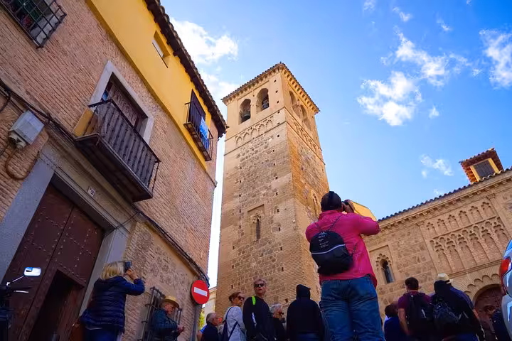 Tourists admire the historic architecture of Toledo on a half-day tour from Madrid, featuring a stone tower against a clear sky.