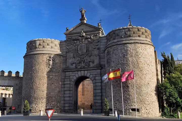 Historic gate in Toledo with flags, a key attraction on the Toledo and Segovia day trip from Madrid.