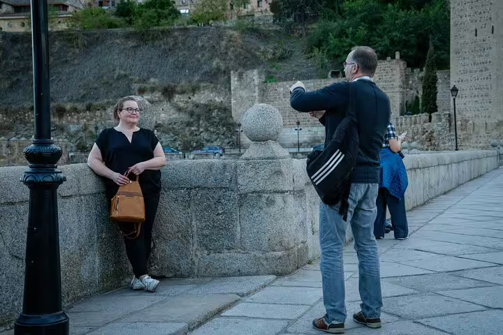 Traveler posing on Toledo stone bridge as guide takes photo, private half-day Toledo minivan tour from Madrid