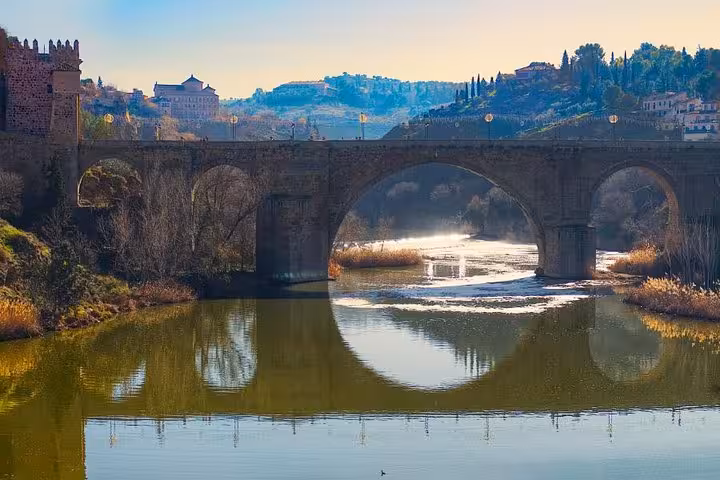 Sunset over the Tagus River with the ancient Alcantara Bridge in Toledo offering a picturesque reflection.