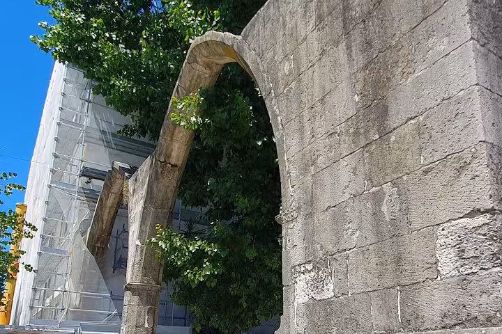 Admire the ancient stone arches of Tomar, showcasing architectural beauty amidst lush greenery and blue skies.