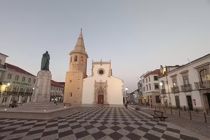 Charming view of the main square in Tomar, Portugal, featuring a historic church and a prominent statue at sunset.