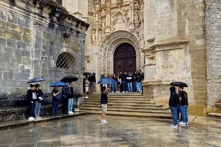 Tour group gathers under umbrellas at the ornate entrance of the Convent of Christ during Tomar walking tour.