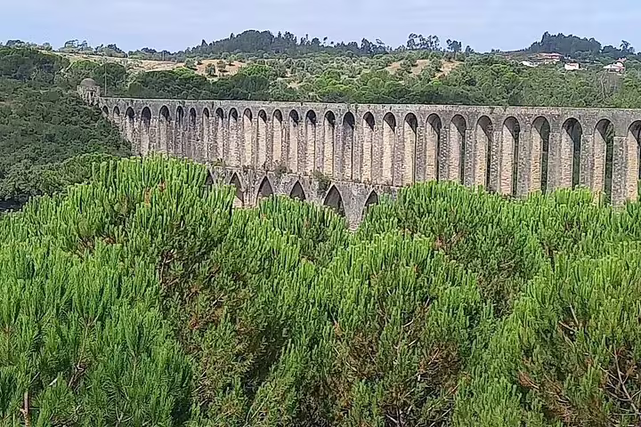 Historic aqueduct in Tomar surrounded by lush greenery, featured in the Tomar-Coimbra tour.
