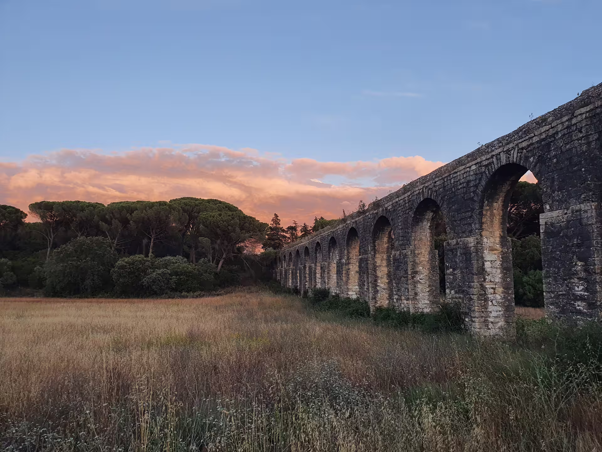 Ancient stone aqueduct in Tomar, Portugal, surrounded by lush greenery and a sunset sky, featured on Knights Templar tour.