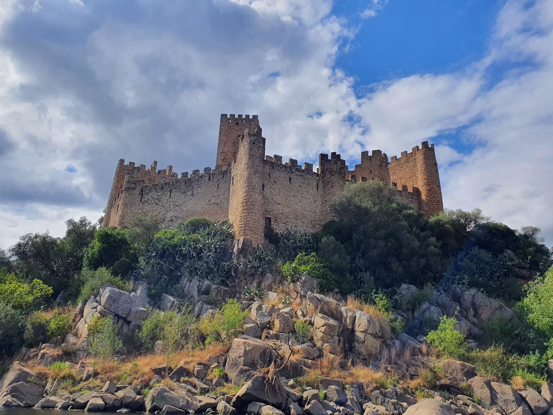 Majestic medieval castle atop a rocky hill with lush greenery under a vibrant blue sky, featured in the Tomar Knights Templar tour.