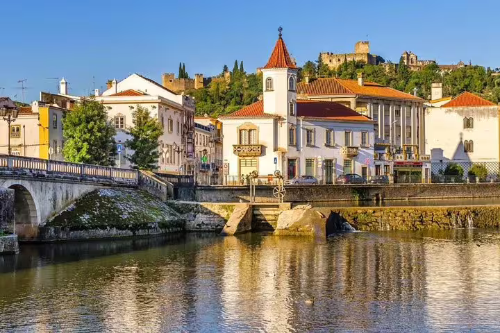 Scenic view of Tomar, Portugal, featuring historic buildings and the Castle of Tomar under a clear blue sky.
