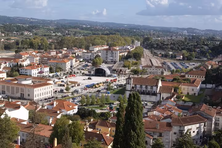 Panoramic view of Tomar, showcasing terracotta-roofed buildings and lush greenery under a clear sky.