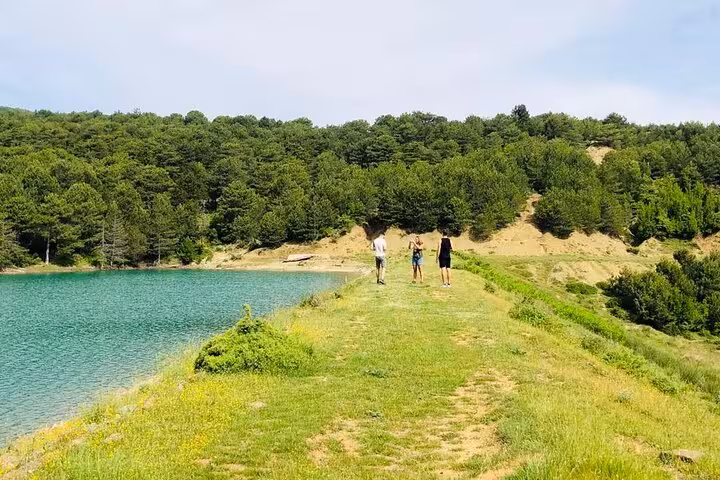 Three hikers walking along a scenic lakeside trail surrounded by lush greenery at Tomor Mountain Lakes in Dardhe.