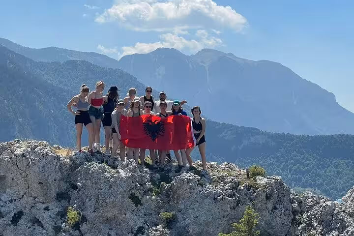 Group holding an Albanian flag atop a mountain with scenic views on the Tomor Mountain Lakes of Dardhe Tour.