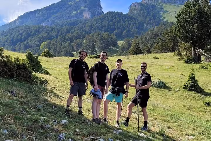 Group of hikers posing on a grassy hillside with a backdrop of majestic mountains at Tomor Mountain Lakes adventure tour.